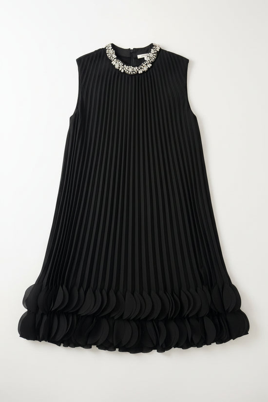 Black pleated dress with embellished neckline on a hanger against a white wall