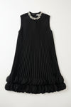 Black pleated dress with embellished neckline on a hanger against a white wall