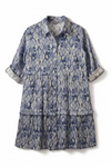 Blue and white patterned dress on a hanger against a beige wall