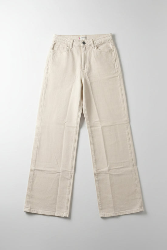 Beige pants hanging on a black hanger against a white wall.