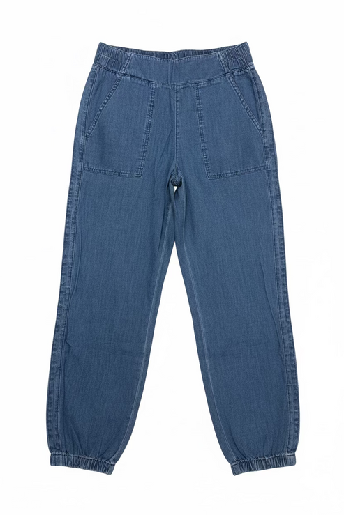 A pair of dark blue denim jogger pants hanging from a black hanger on a wall rack, positioned above a wooden bench against a textured off-white wall.