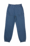 A pair of dark blue denim jogger pants hanging from a black hanger on a wall rack, positioned above a wooden bench against a textured off-white wall.
