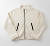 An off-white textured zip-up jacket with black zipper details, hanging on a black hanger against a white paneled door.