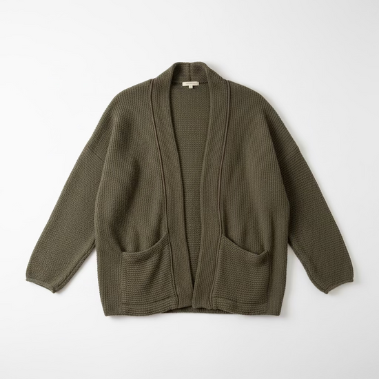 An olive green waffle-knit open-front cardigan sweater hanging on a black hanger against a textured off-white wall.