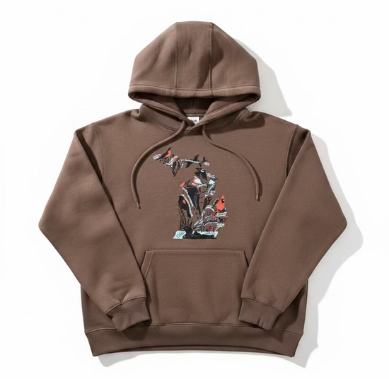 A brown pullover hoodie with a graphic print of birds and branches, laid flat on a beige branded paper surface over a wooden floor.