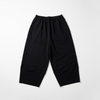 Black wide-leg cropped pants hanging on a black hanger from a wall rack, with a light-colored textured wall and wooden bench visible in the background.