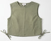 Green sleeveless vest hanging on a hanger against a white wall