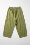 Green baggy pants hanging on a hanger against a white wall