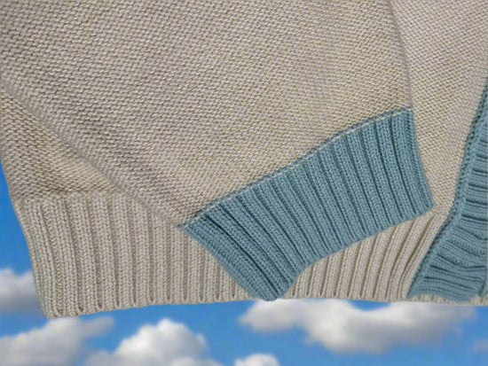 Close-up of a beige sweater with blue ribbed cuffs and hem on a light gray background