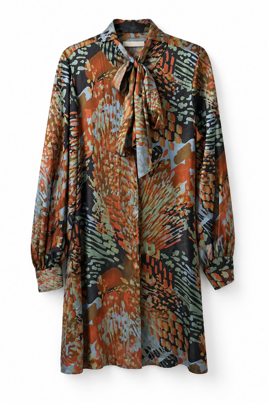 A long-sleeve silk-like blouse with a tie-neck collar, featuring an abstract, painterly pattern in rust orange, brown, black, gray, and muted blue. A white tag is attached near the collar, and the blouse is hanging against a textured off-white wall.